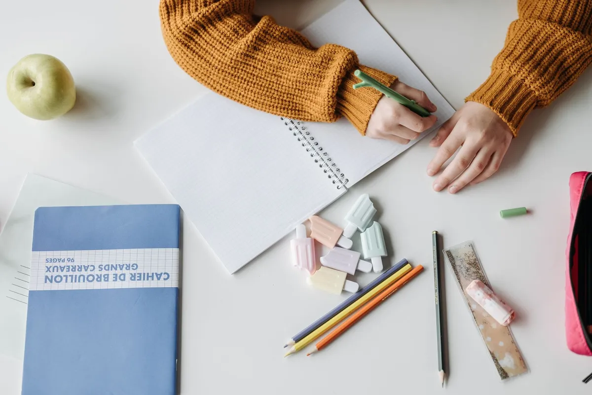A child writing in a notebook surrounded by school supplies
