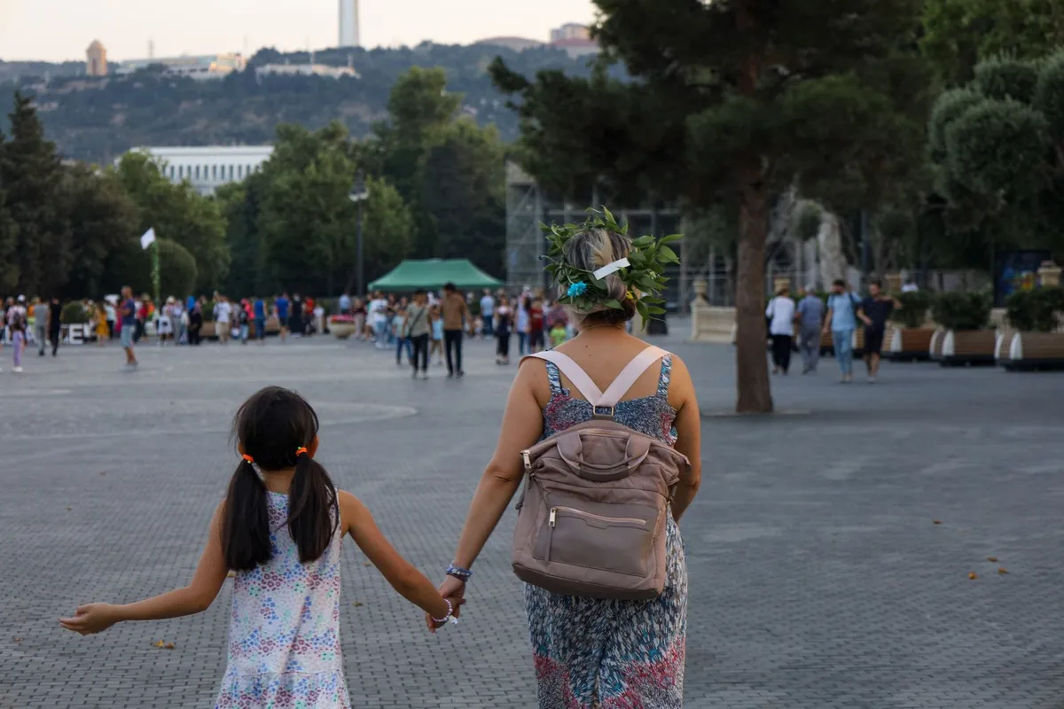 A mother holding her daughter's hand as they walk together, seen from behind