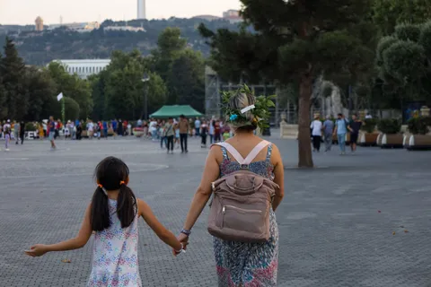 A mother holding her daughter's hand as they walk together, seen from behind