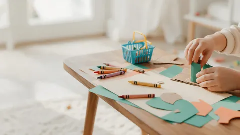 A child's hands building a paper and cardboard craft on a wooden table with crayons and a small basket