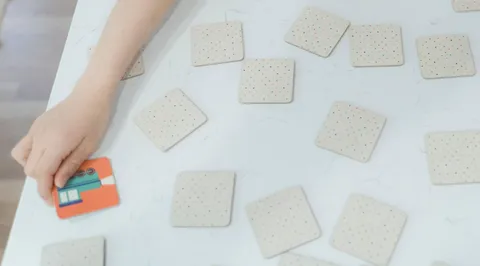 A child's hand turning over a memory card among cards laid out on a white table