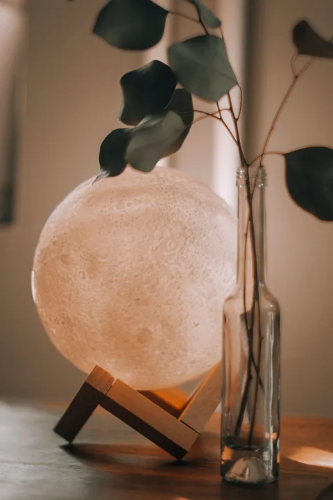 A glowing moon lamp beside a glass vase in a cozy room