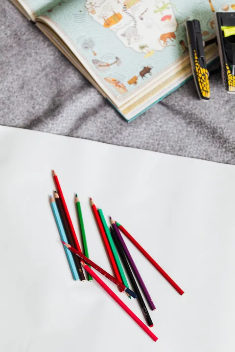 Colored pencils on white paper beside an open book