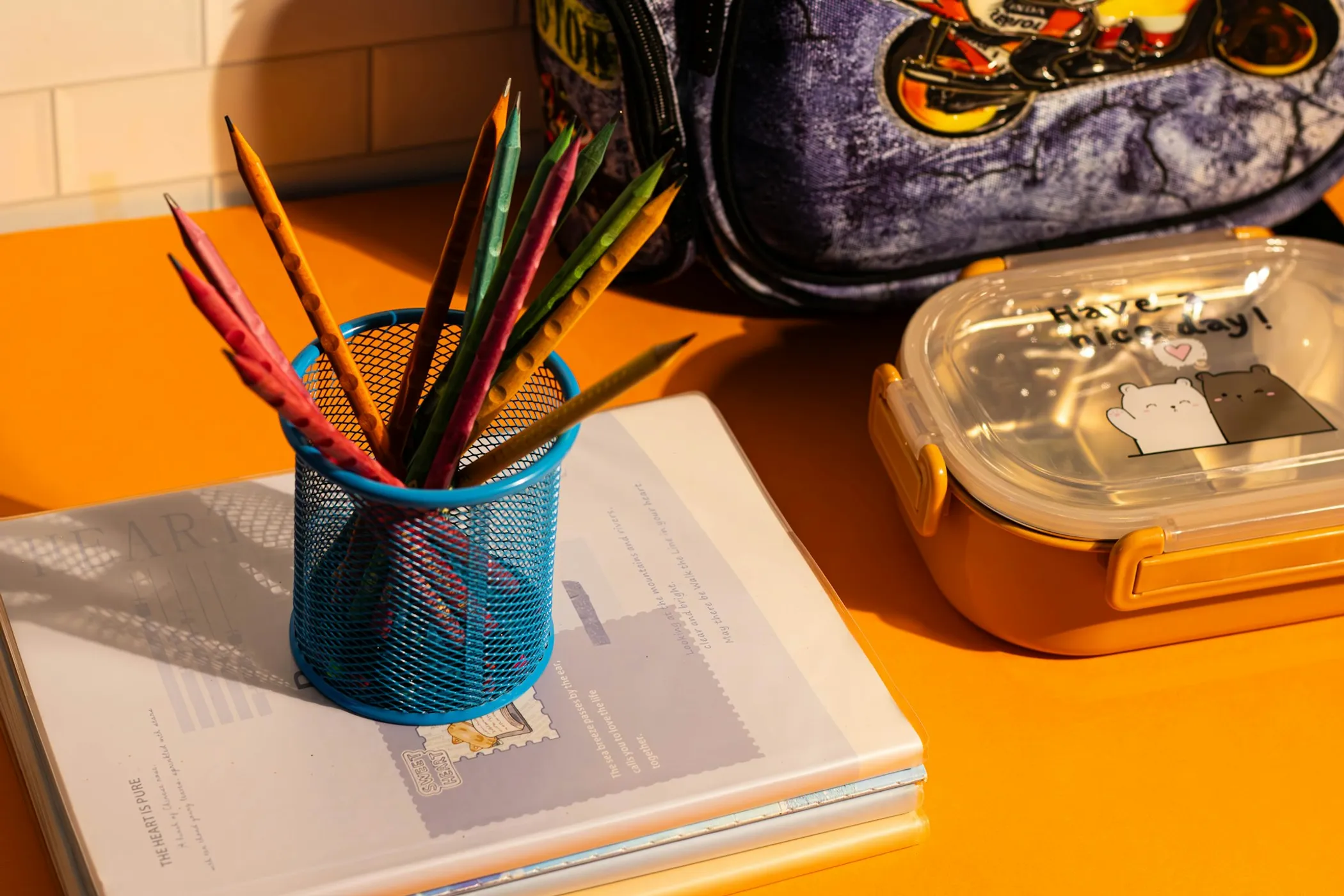 Pencil cup, school backpack and lunchbox on an orange desk