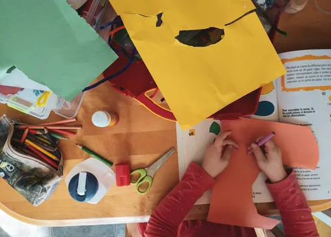 A child's hands cutting and coloring paper on a craft table