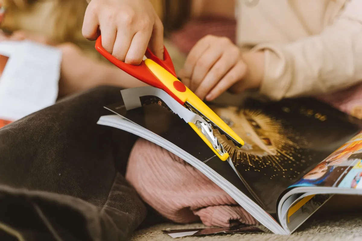 Close-up of a child cutting a magazine page with scissors