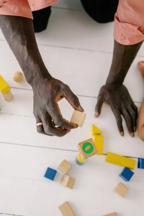 Hands arranging colorful wooden blocks on a white floor