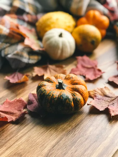 A small striped pumpkin surrounded by autumn leaves