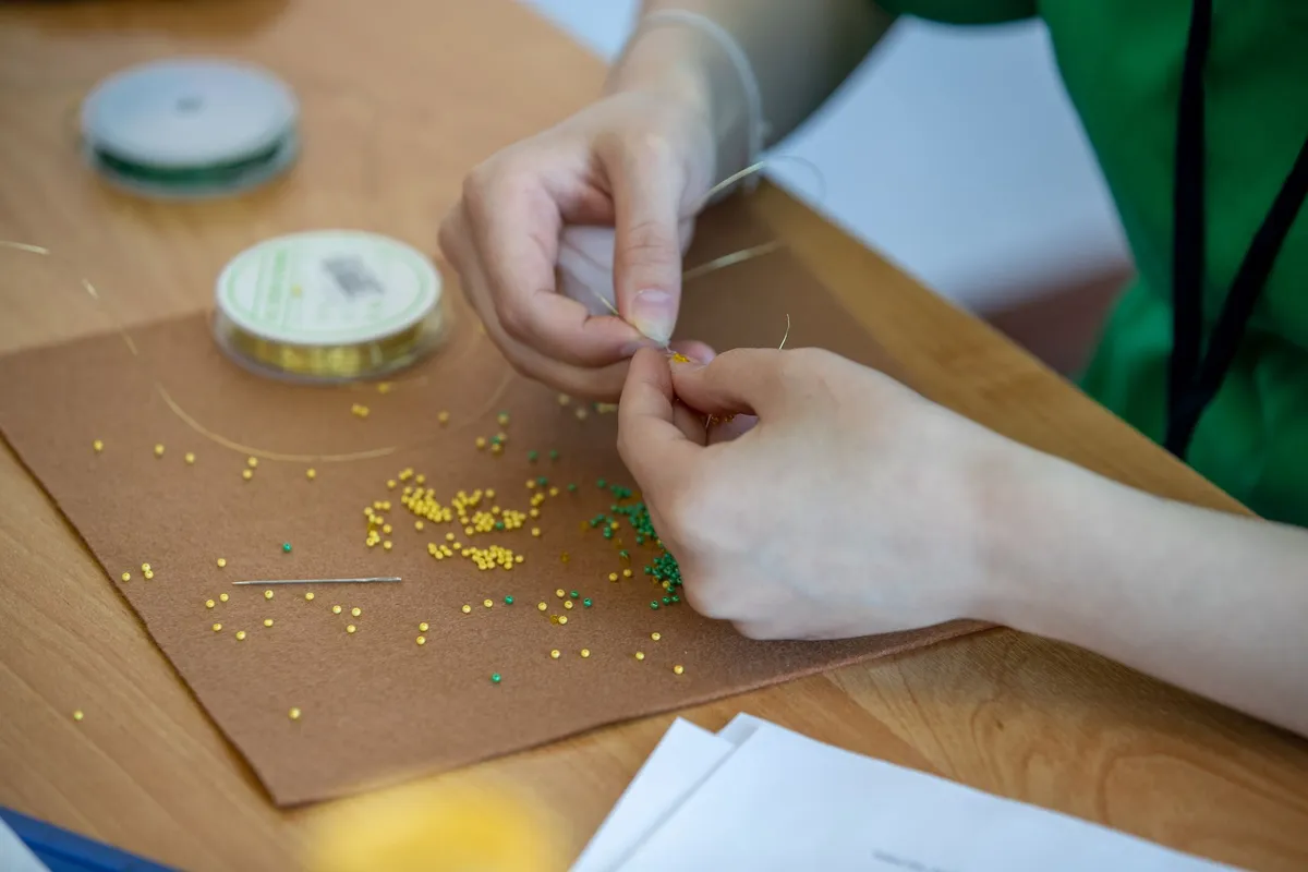 Hands stringing green and yellow beads