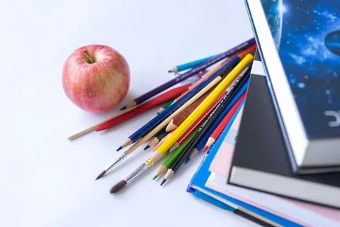 Colorful school supplies arranged with an apple on a white surface