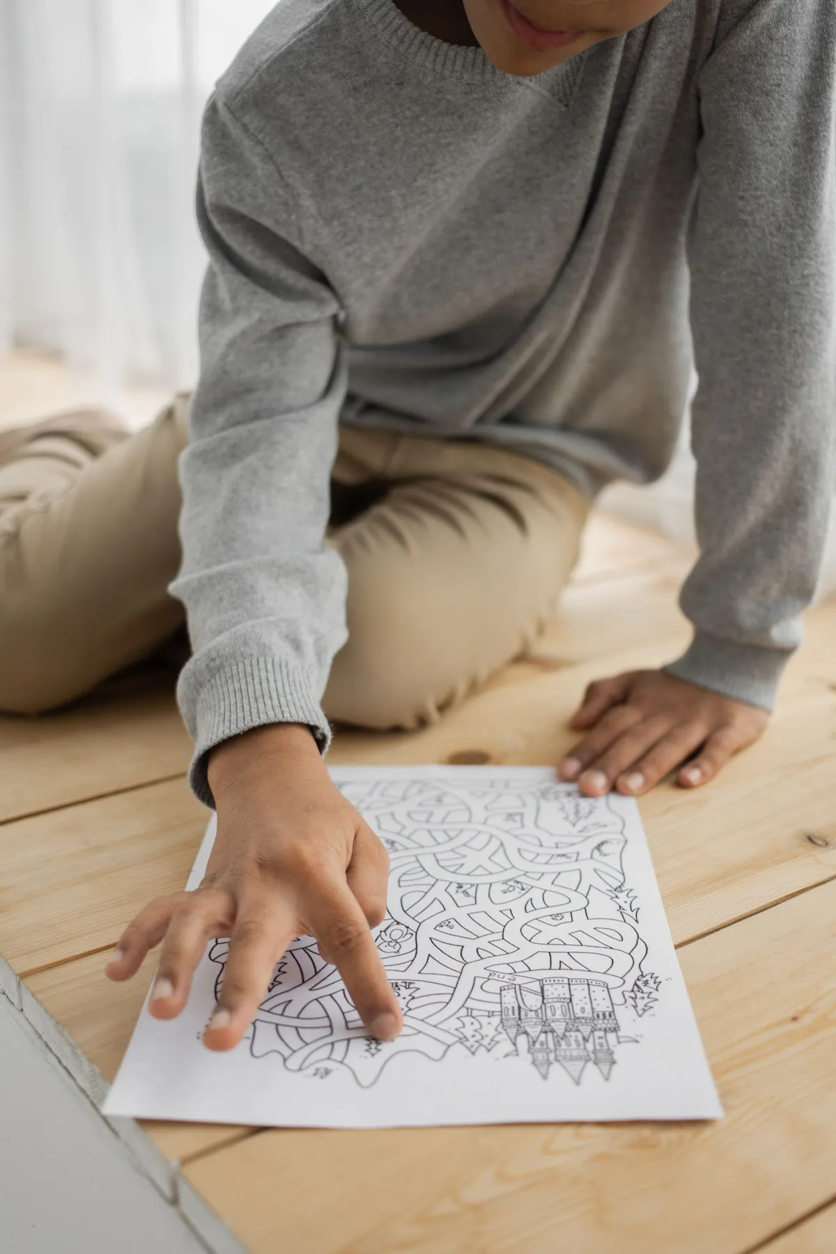 A child sitting on the floor solving a maze puzzle, seen from above