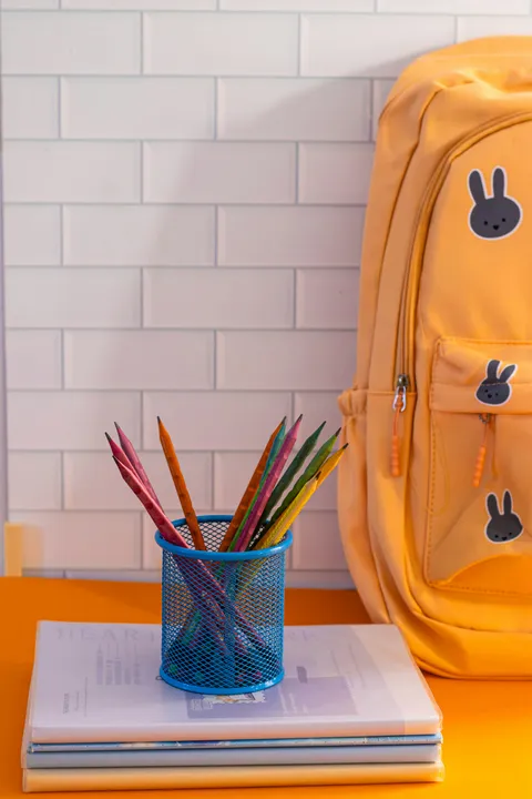 Orange school backpack beside a cup of colored pencils