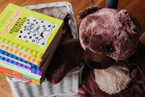 A stack of colorful children's books beside a plush teddy bear