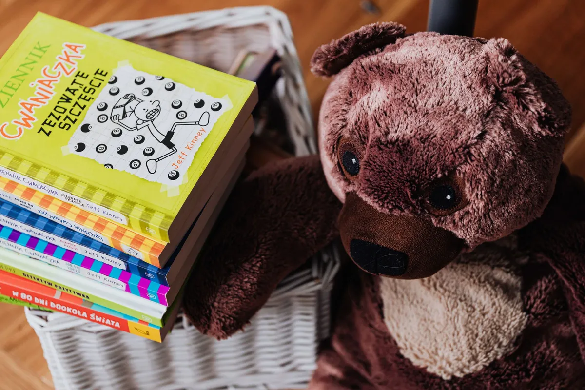A stack of colorful children's books beside a plush teddy bear