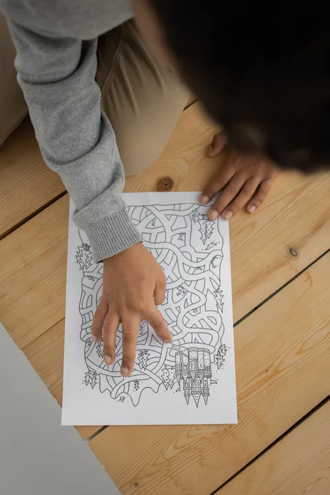 A child sitting on the floor solving a maze puzzle, seen from above