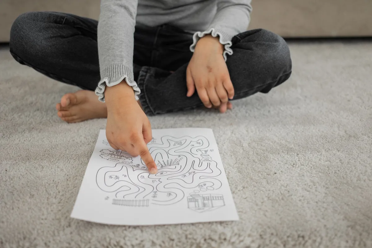A barefoot child sitting cross-legged on the floor working on a page