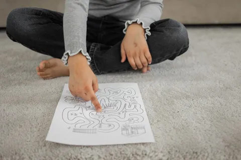 A barefoot child sitting cross-legged on the floor working on a page