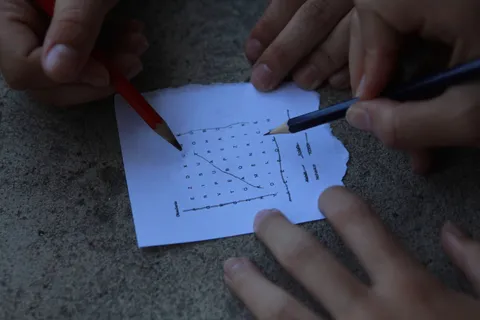 Hands using pencils to solve a word puzzle on paper