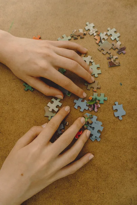 Hands sorting colorful jigsaw puzzle pieces on a wooden surface