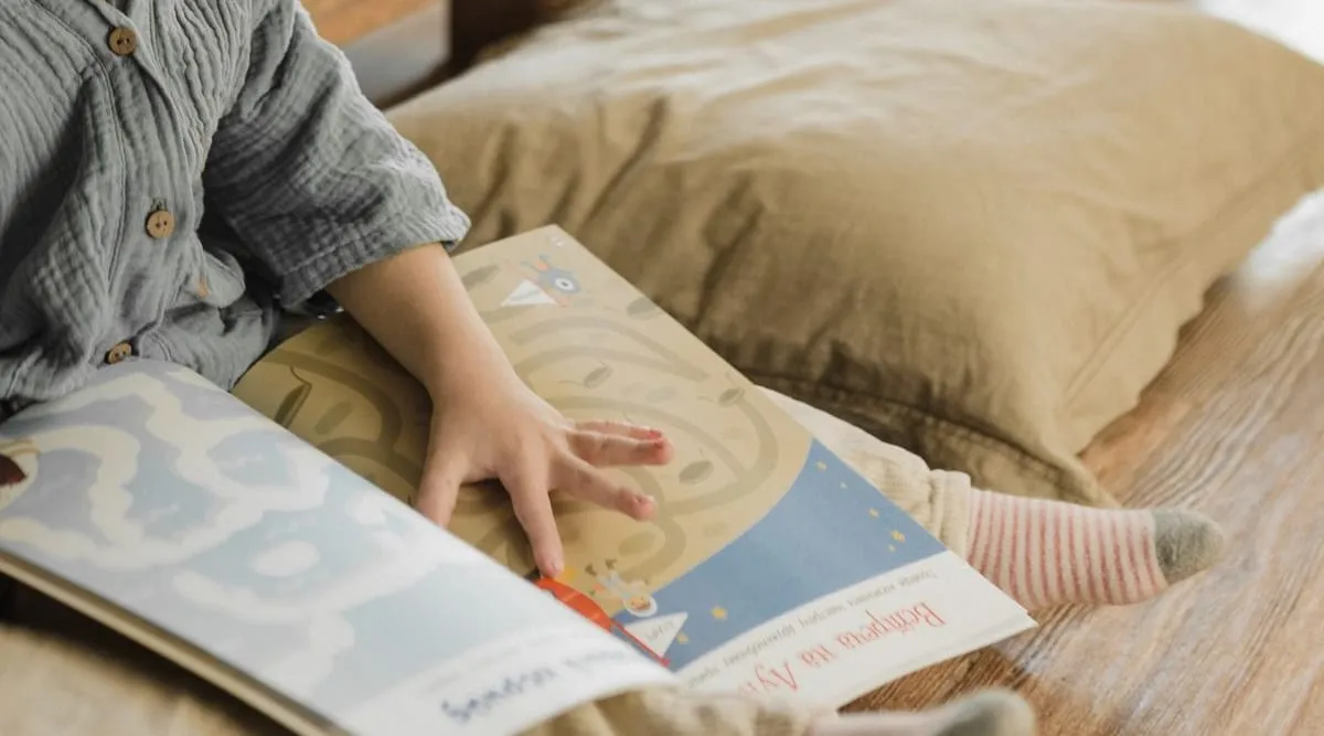 A child's hand resting on an open picture book on a cushion