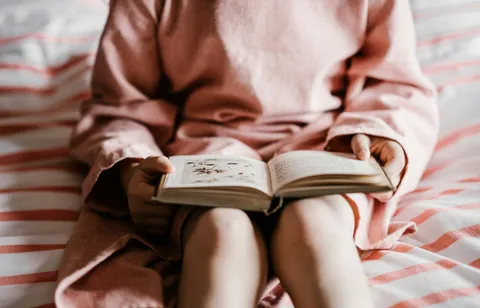 A child sitting on a bed reading an open book