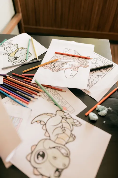 An assortment of kids' coloring pages and pencils on a desk