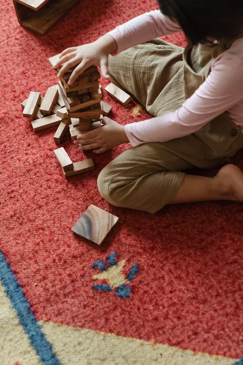 A child sitting barefoot on a carpet playing with toys, seen from above
