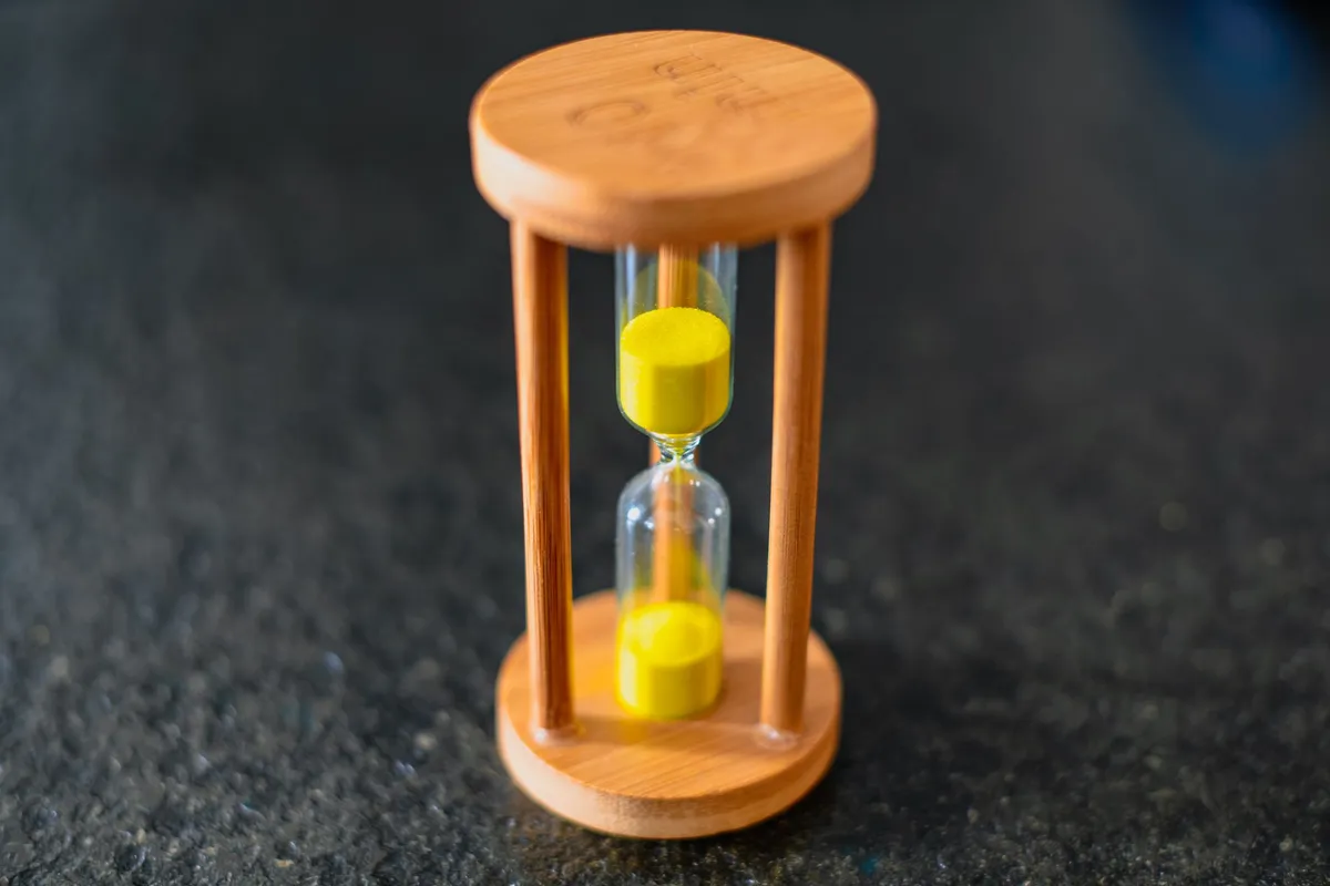 A wooden hourglass with yellow sand on a dark surface