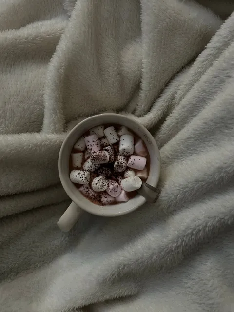 A cup of hot chocolate with marshmallows on a soft blanket